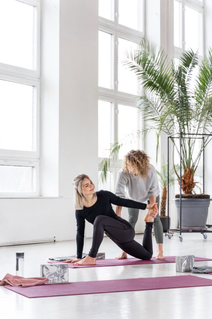 yoga instructor helping a student with yoga pose. Instructor is happy that she has specialized bookkeeping for yoga studios in her corner